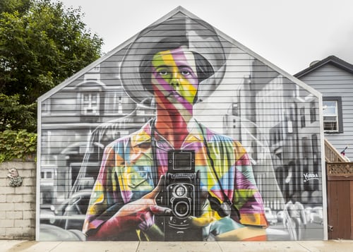 man holding camera painting on side of house